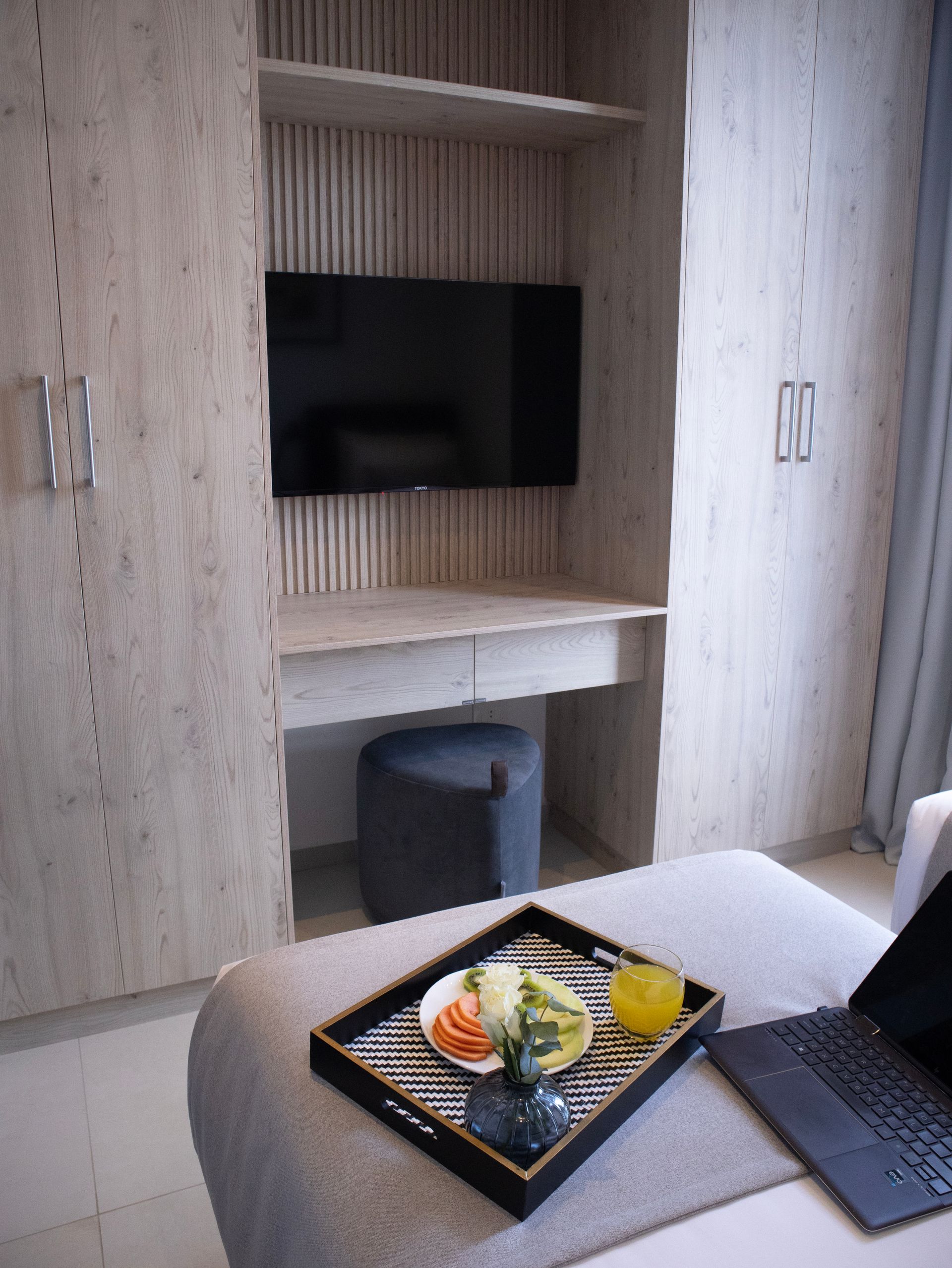 Dormitorio con armarios empotrados, TV, escritorio y bandeja con comida sobre una cama.