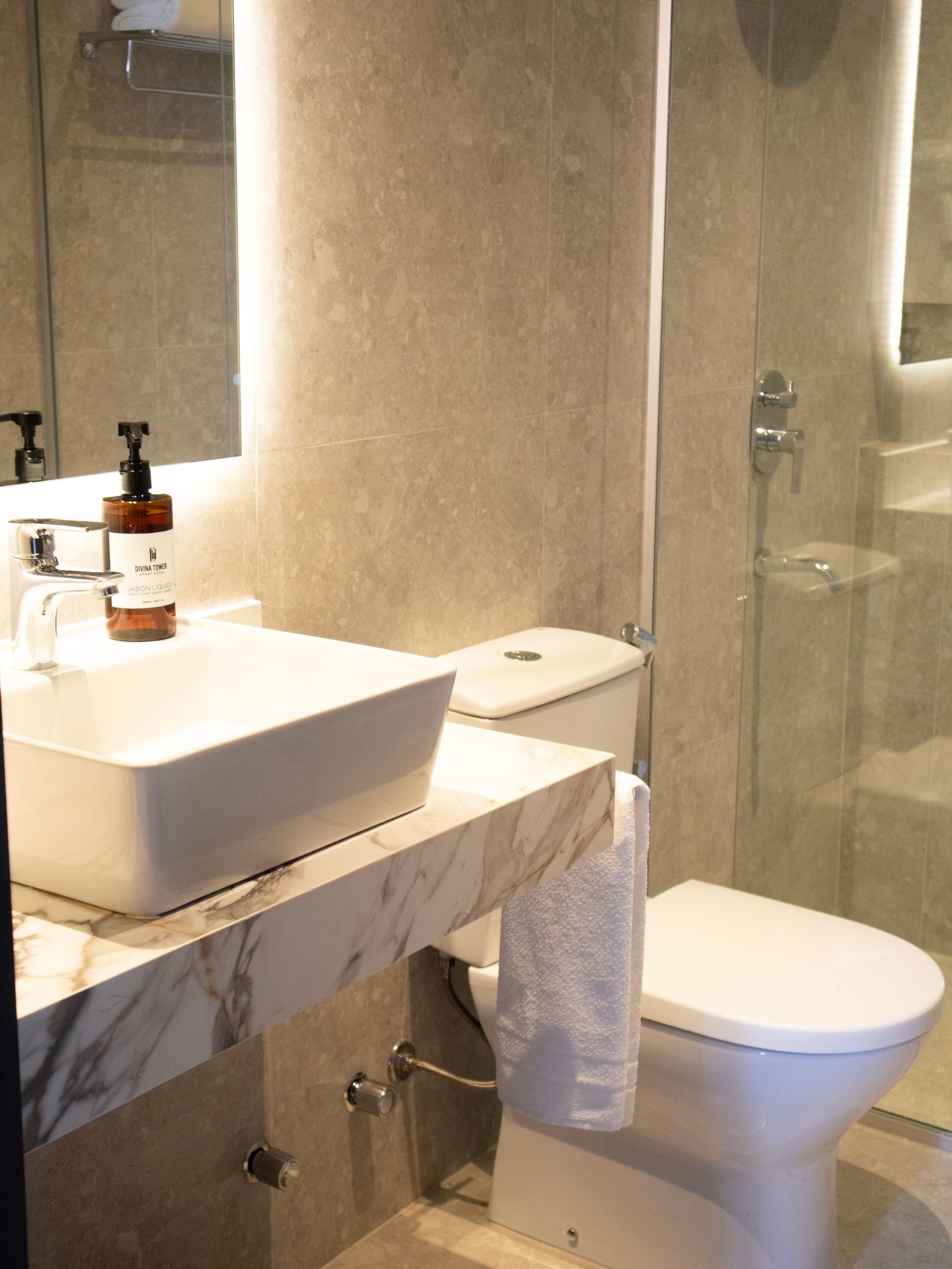 Baño moderno con lavabo, inodoro y ducha de cristal. Paredes grises y encimera de mármol.