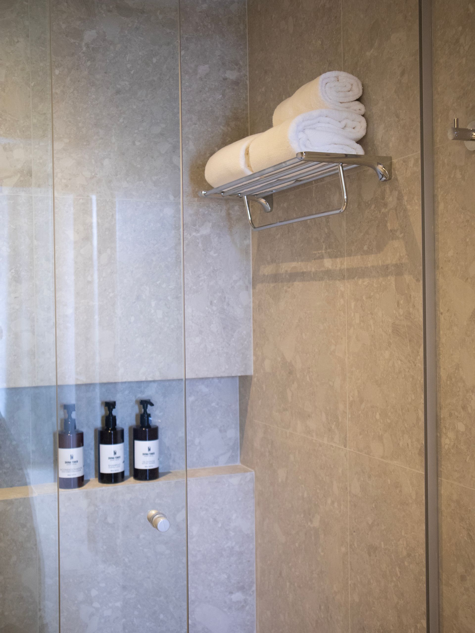 Baño con pila de toallas blancas, botellas de champú y puerta de ducha.