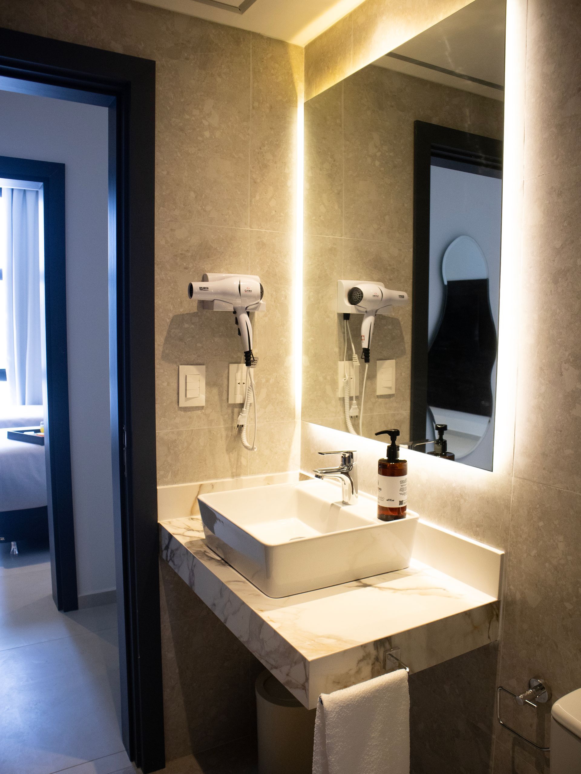 Baño moderno con paredes grises, lavabo cuadrado, espejo iluminado y secador de pelo.