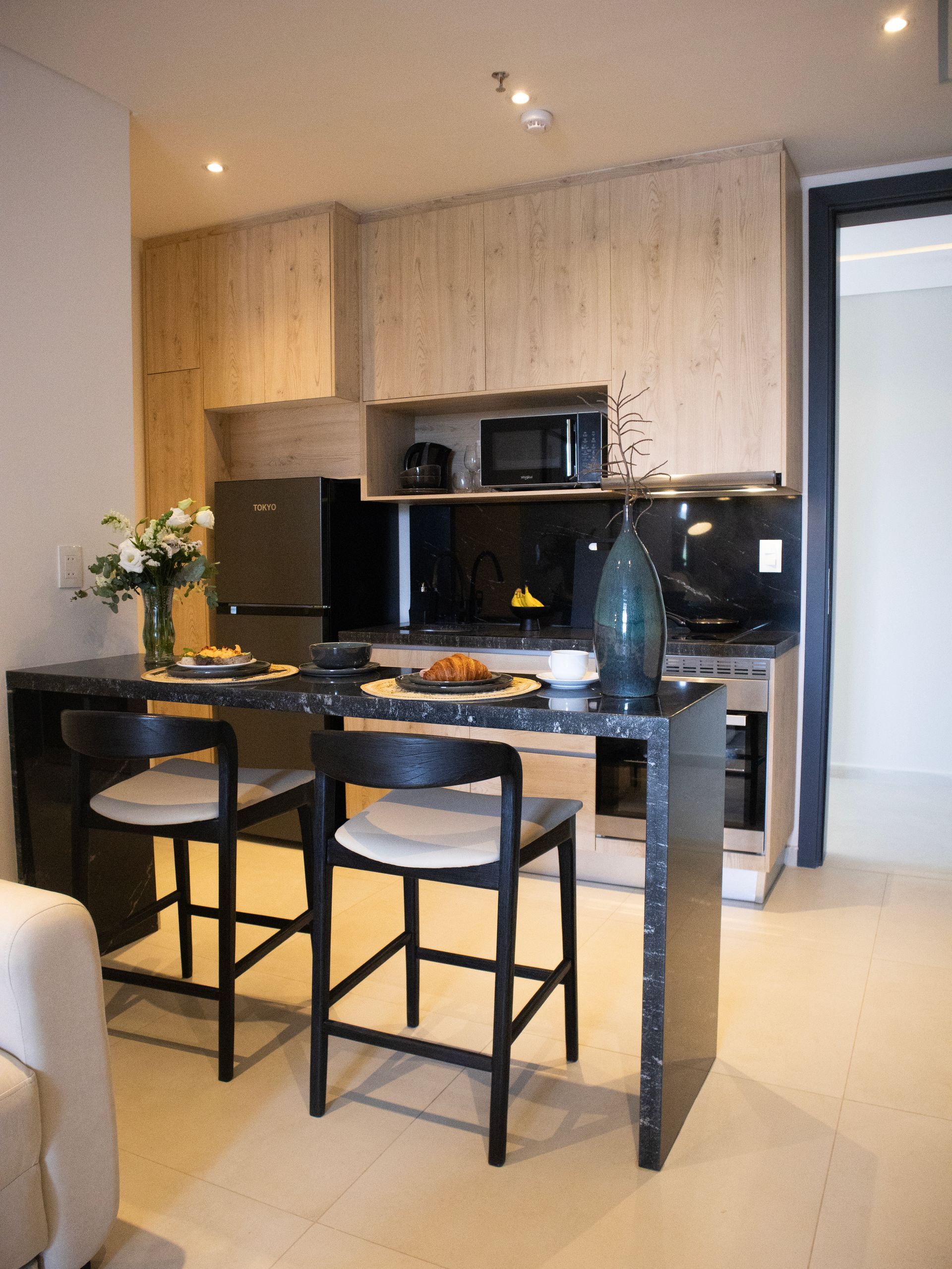 Cocina moderna con barra de desayuno, dos taburetes y electrodomésticos de acero inoxidable.