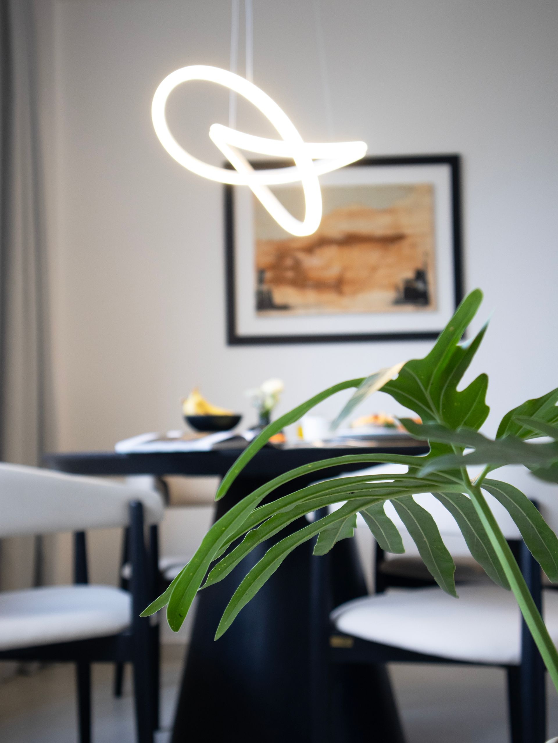Comedor moderno: mesa y sillas negras, obras de arte y una singular lámpara colgante LED con espirales.