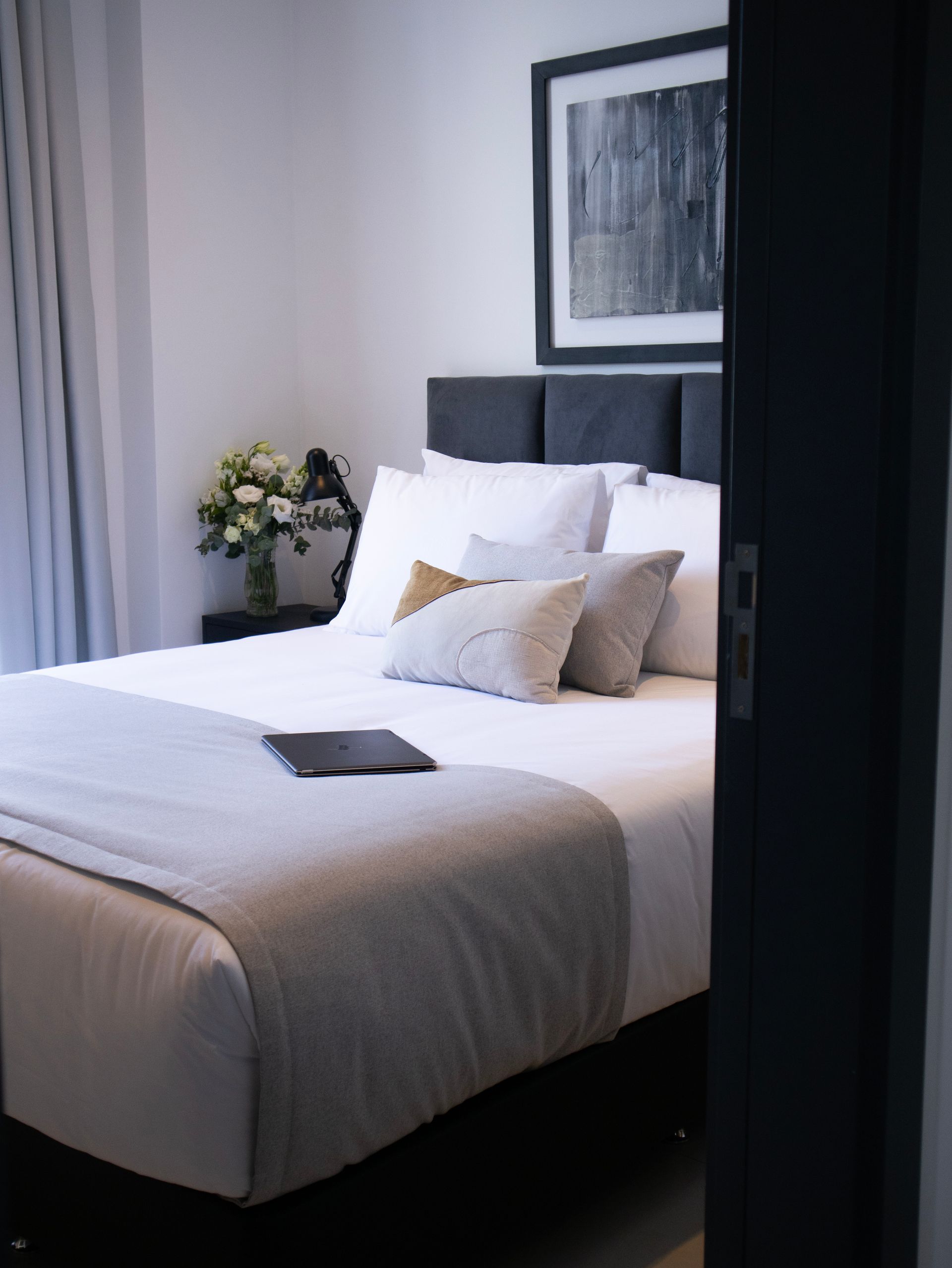 Dormitorio con cama, almohadas, manta y obras de arte. Combinación de colores gris y blanco.