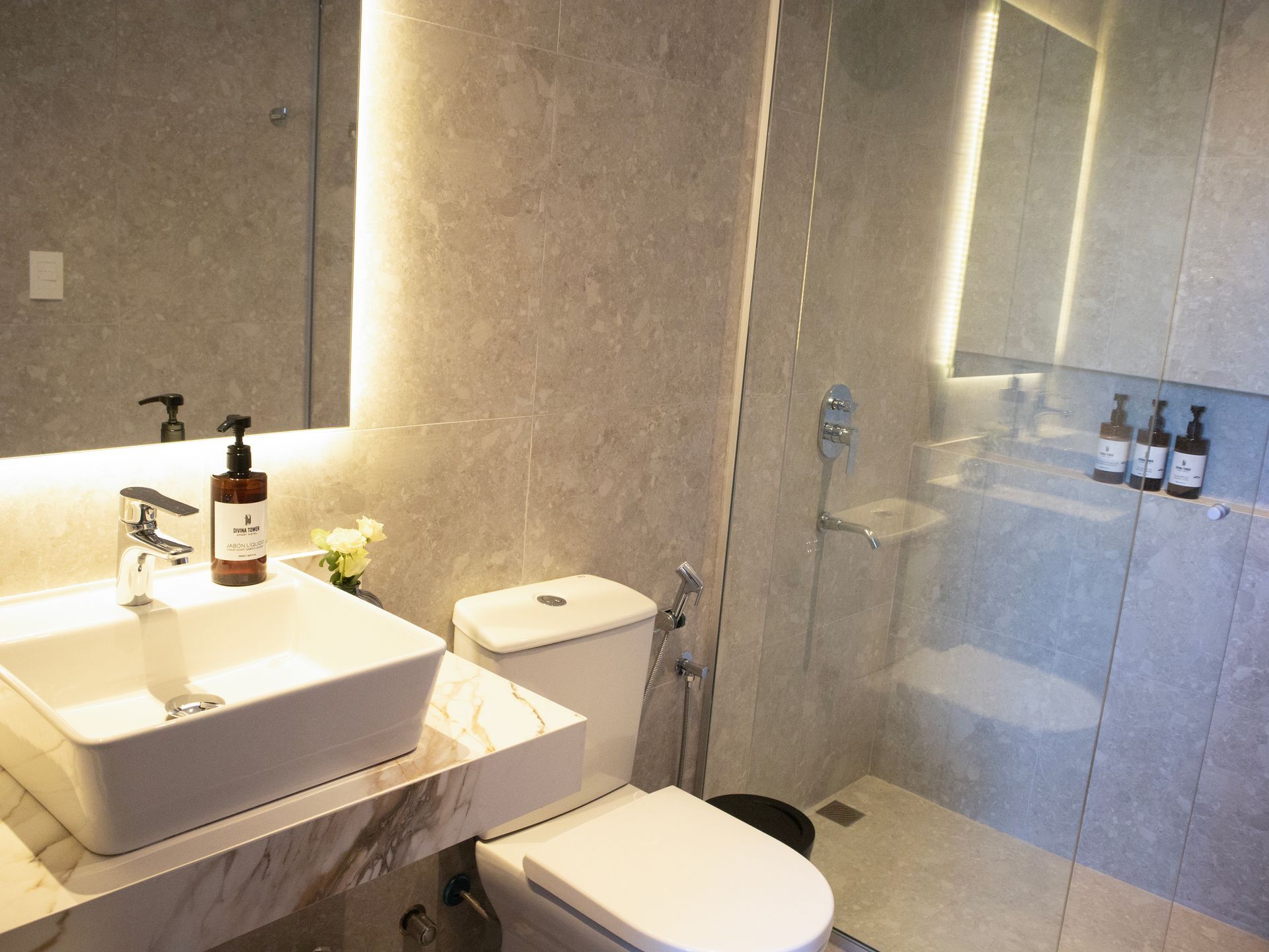 Baño moderno con lavabo cuadrado, inodoro, ducha de cristal, azulejos grises.