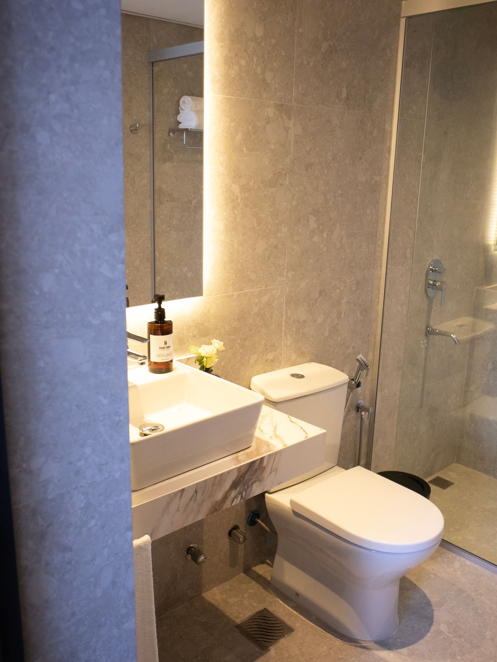 Baño moderno con lavabo e inodoro blancos, paredes grises y ducha de cristal.