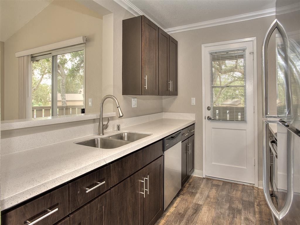 Modern apartment kitchen with dark wood cabinets, white countertops, and stainless appliances.