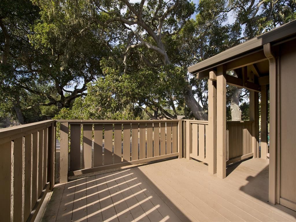 Wooden balcony deck with railing and trees beyond.