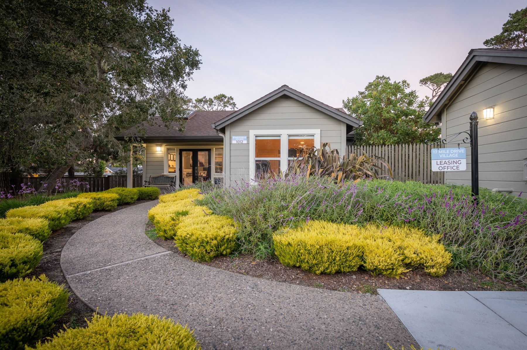 Exterior view of a leasing office with a curved walkway and yellow shrubs