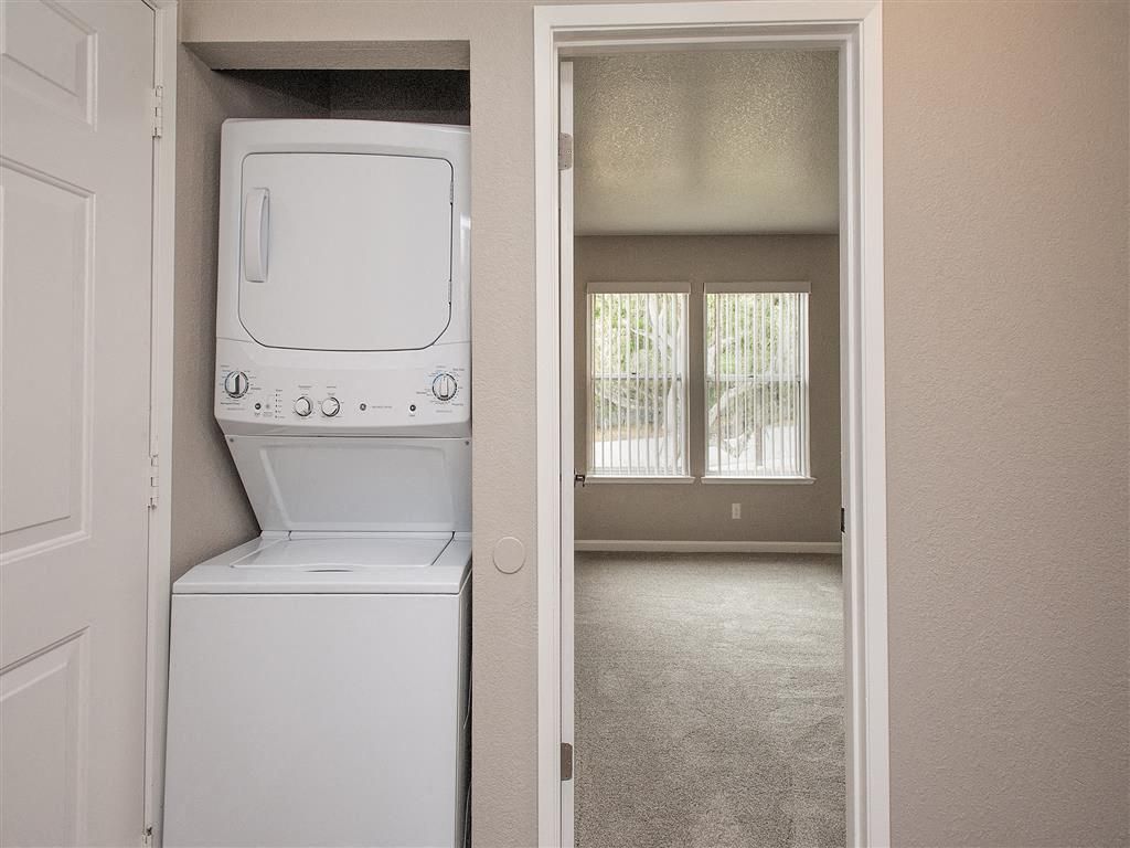 Stacked washer and dryer in a closet beside a doorway to a carpeted living area.