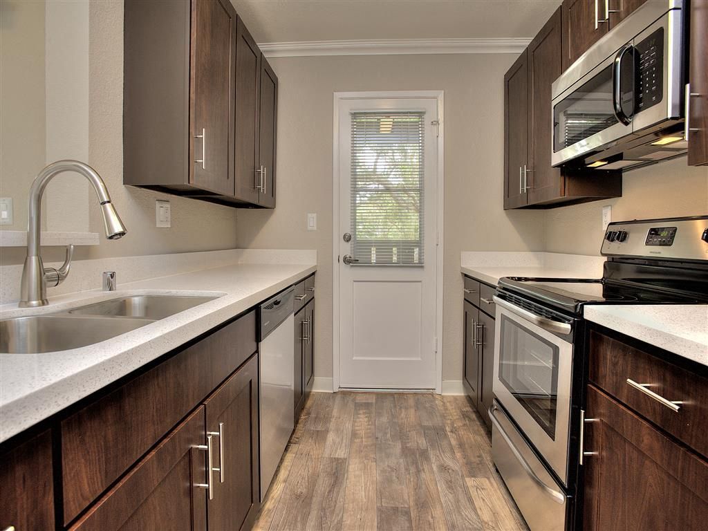 Galley kitchen with dark wood cabinets, white countertops, and stainless steel appliances.