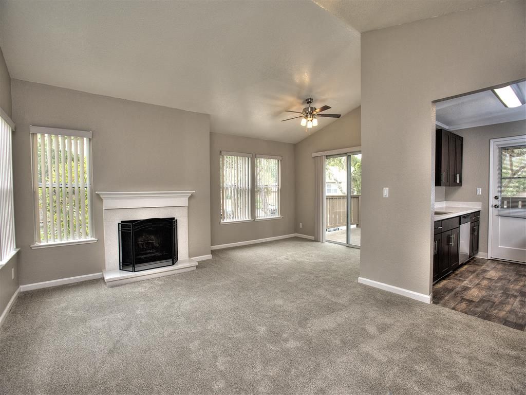 Living room with fireplace, large windows, ceiling fan, and open kitchen.