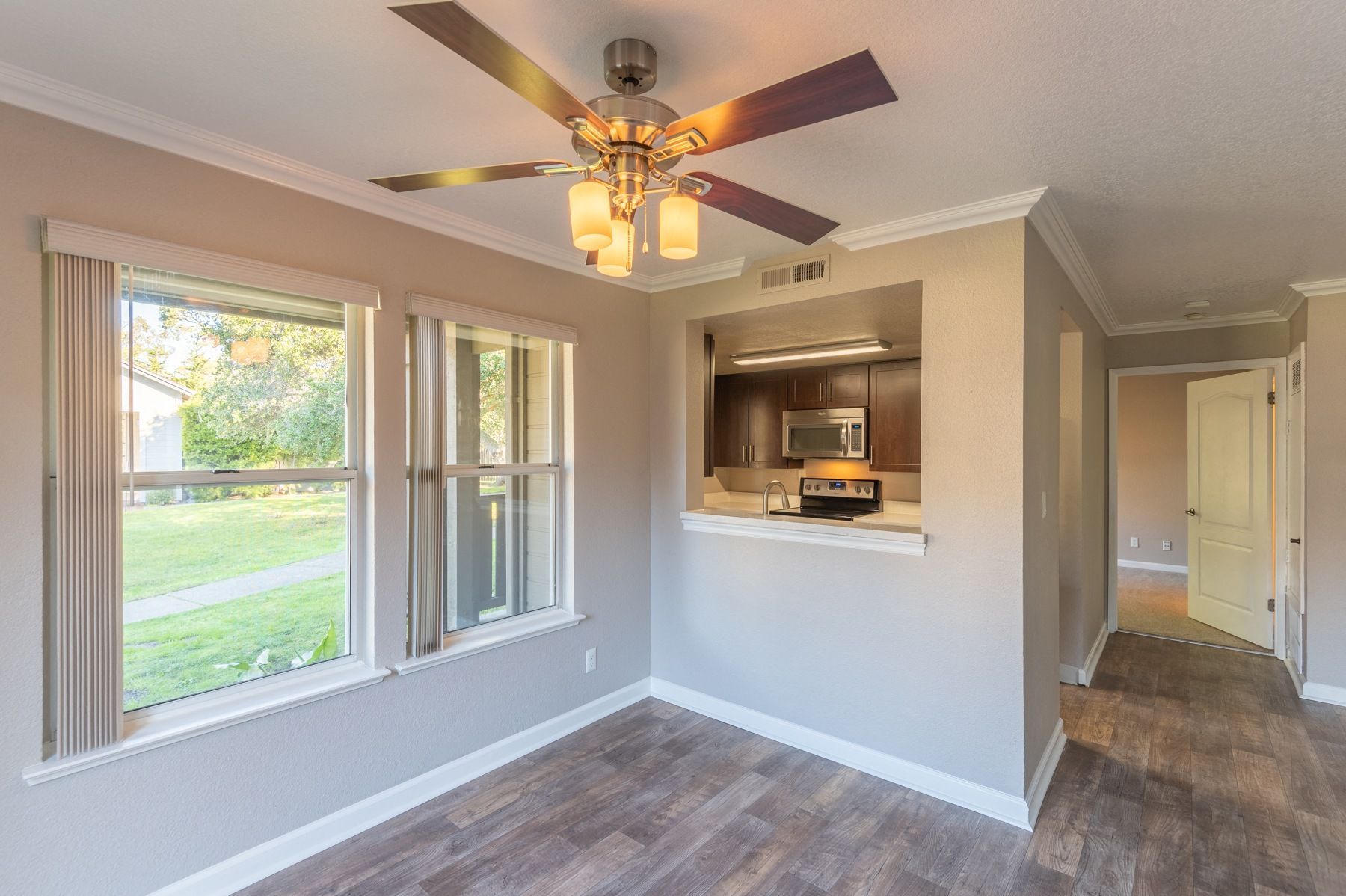 Living area with a ceiling fan, large windows, and a kitchen pass-through.