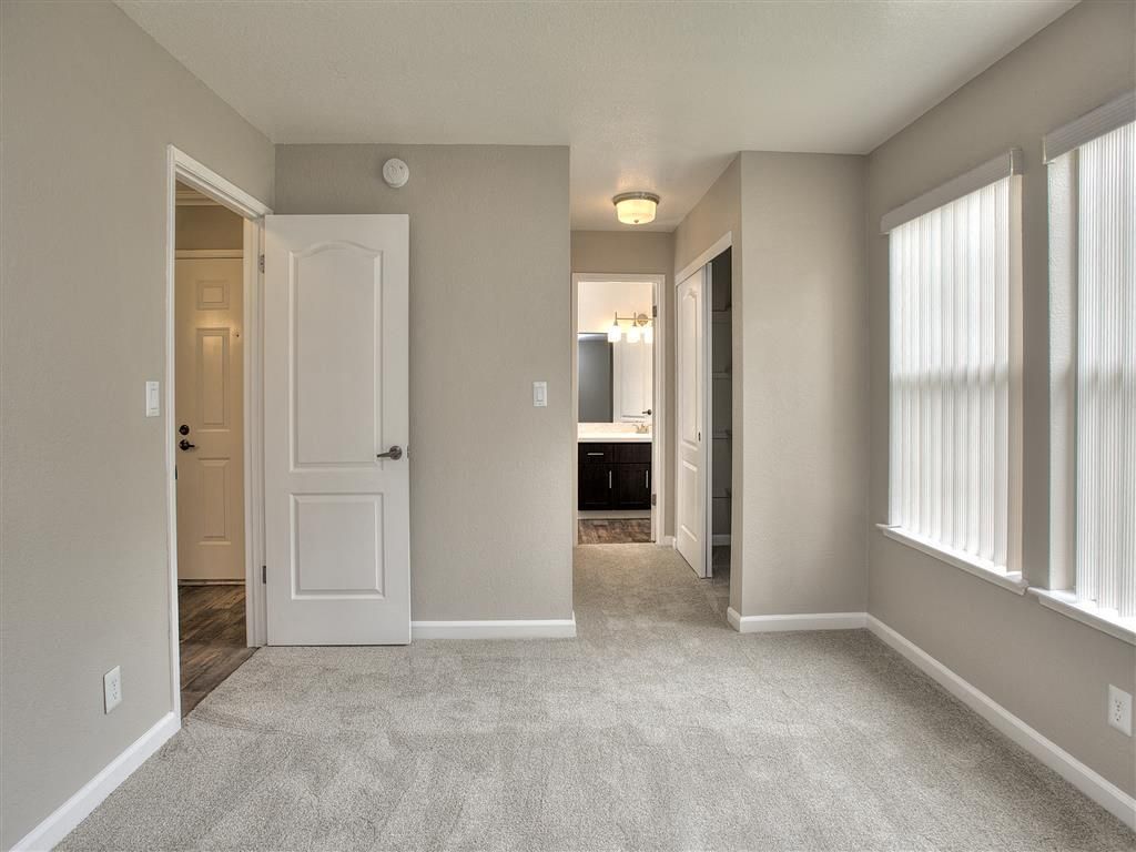 Interior apartment room with carpet, neutral walls, and a doorway to the bathroom.