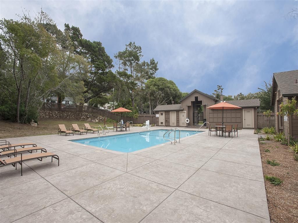 Outdoor community pool area with lounge chairs and umbrellas.