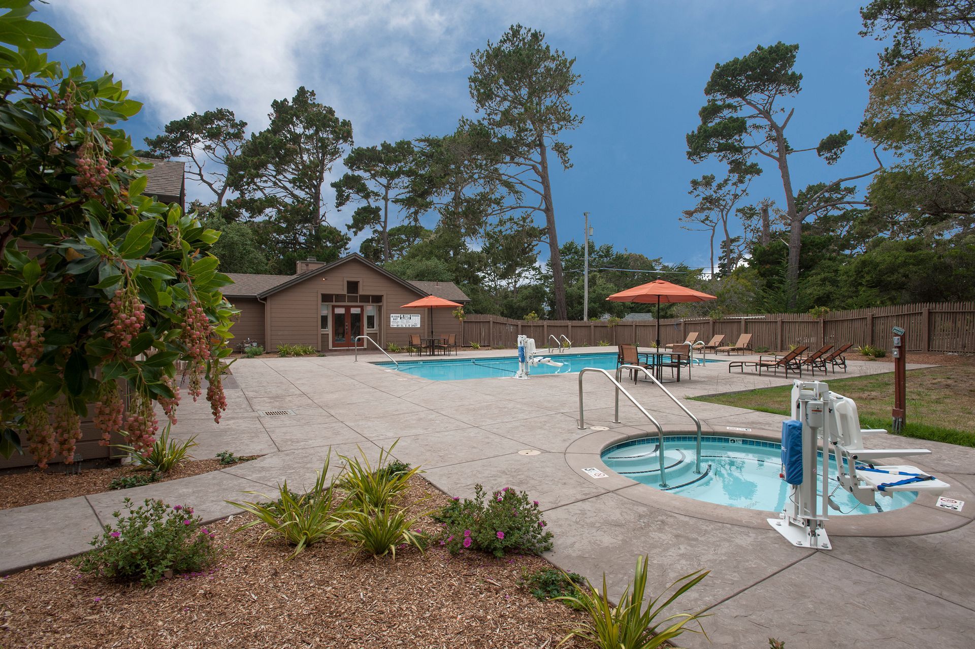 Outdoor pool area at a multifamily community with seating, umbrellas, and a pool house.