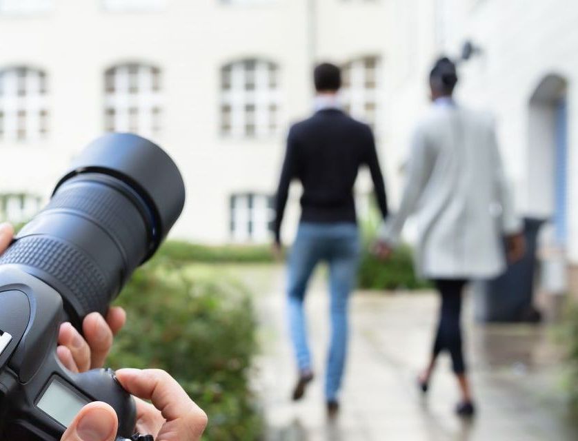 A person is taking a picture of a couple walking down a sidewalk.