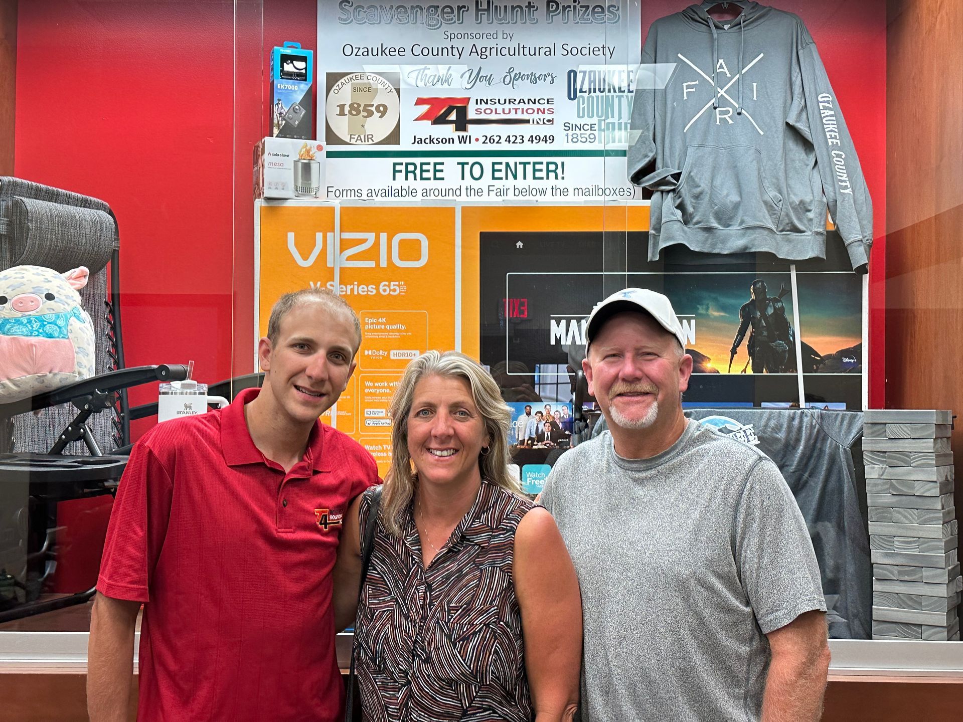 T4 Insurance team pose in front of a prize display. A Vizio TV and other prizes are visible.