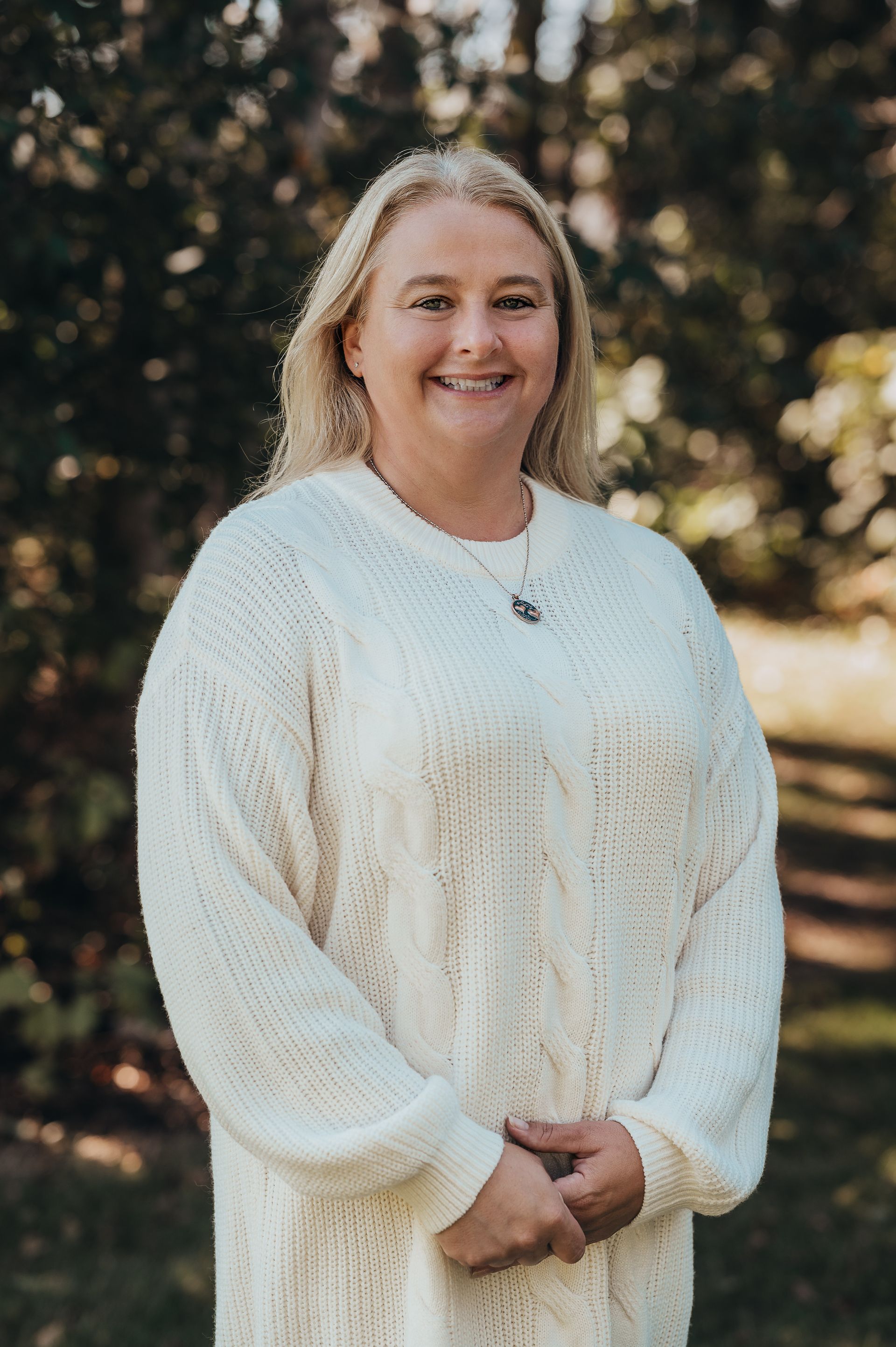 Woman with blonde hair, wearing a white sweater, smiling, outdoors.