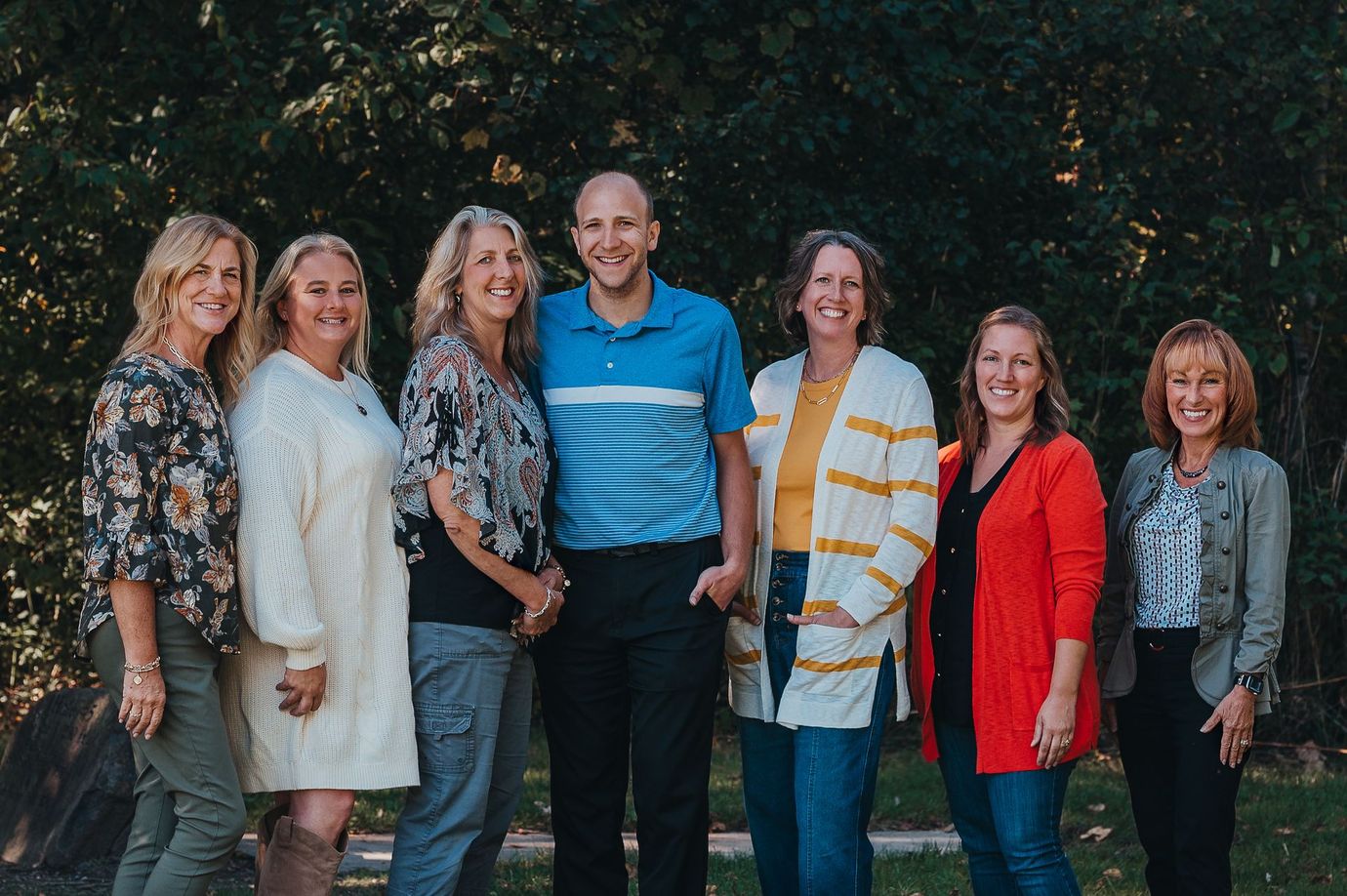Group of seven people smiling outdoors.