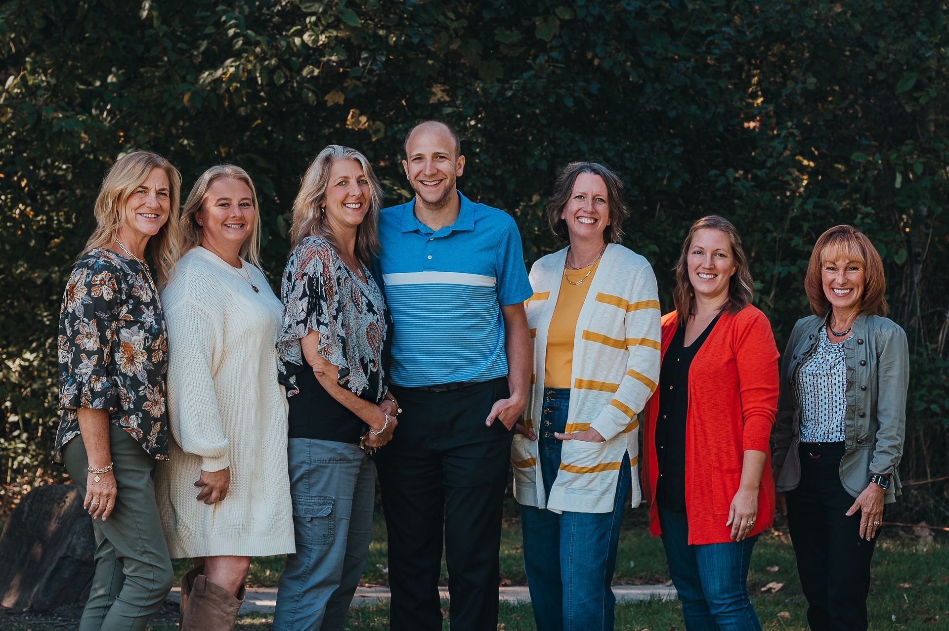 Group of seven people smiling outdoors.