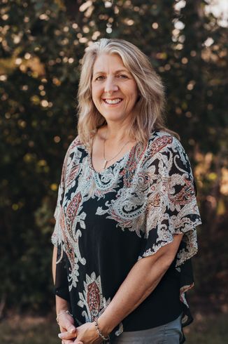 Woman with blonde hair wearing a patterned top, smiling outdoors.