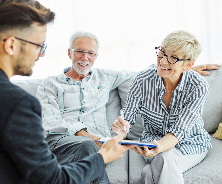 A financial advisor reviews paperwork with an older couple on a couch.