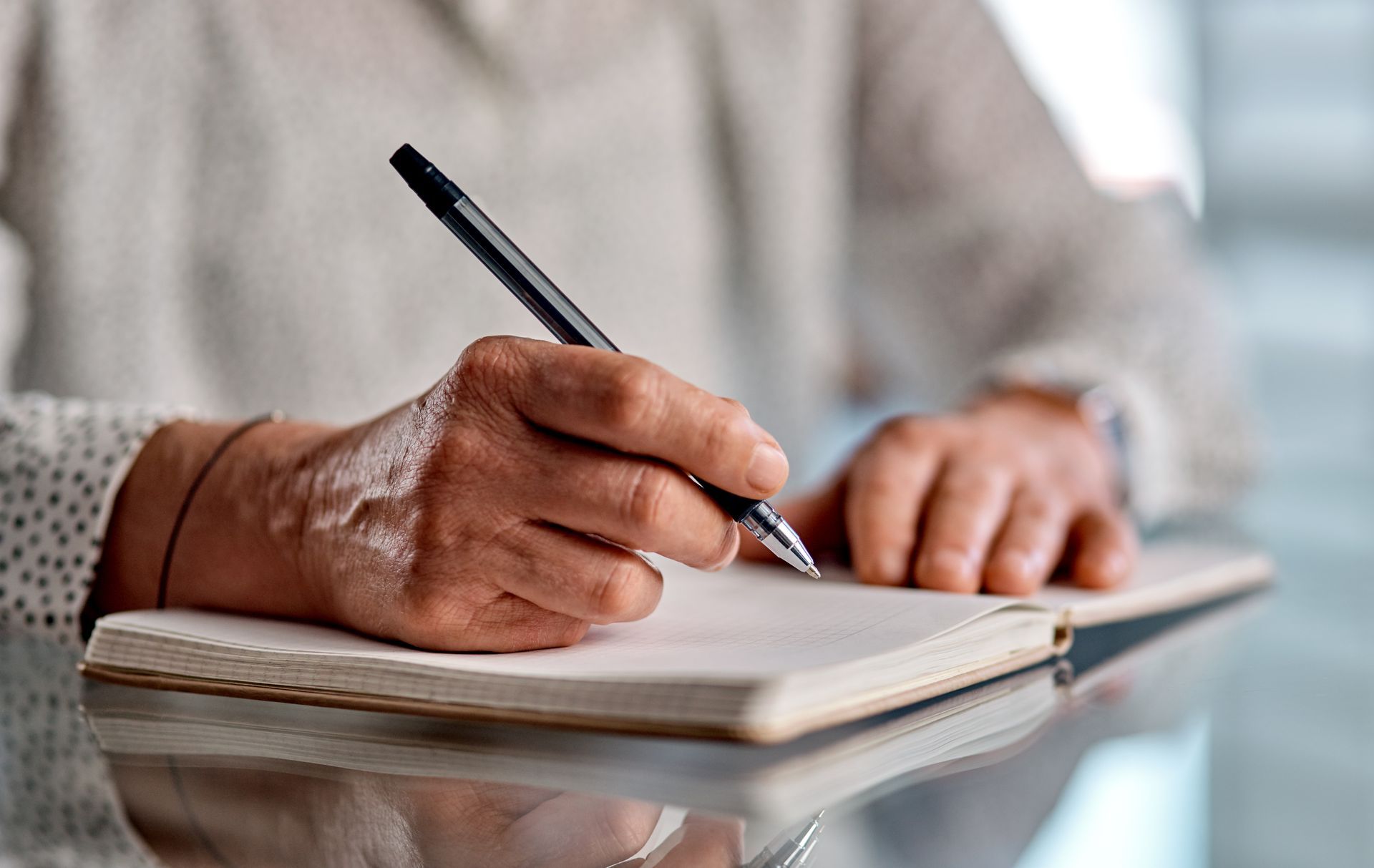 Person's hand writing with a black pen in a notebook. Light background.