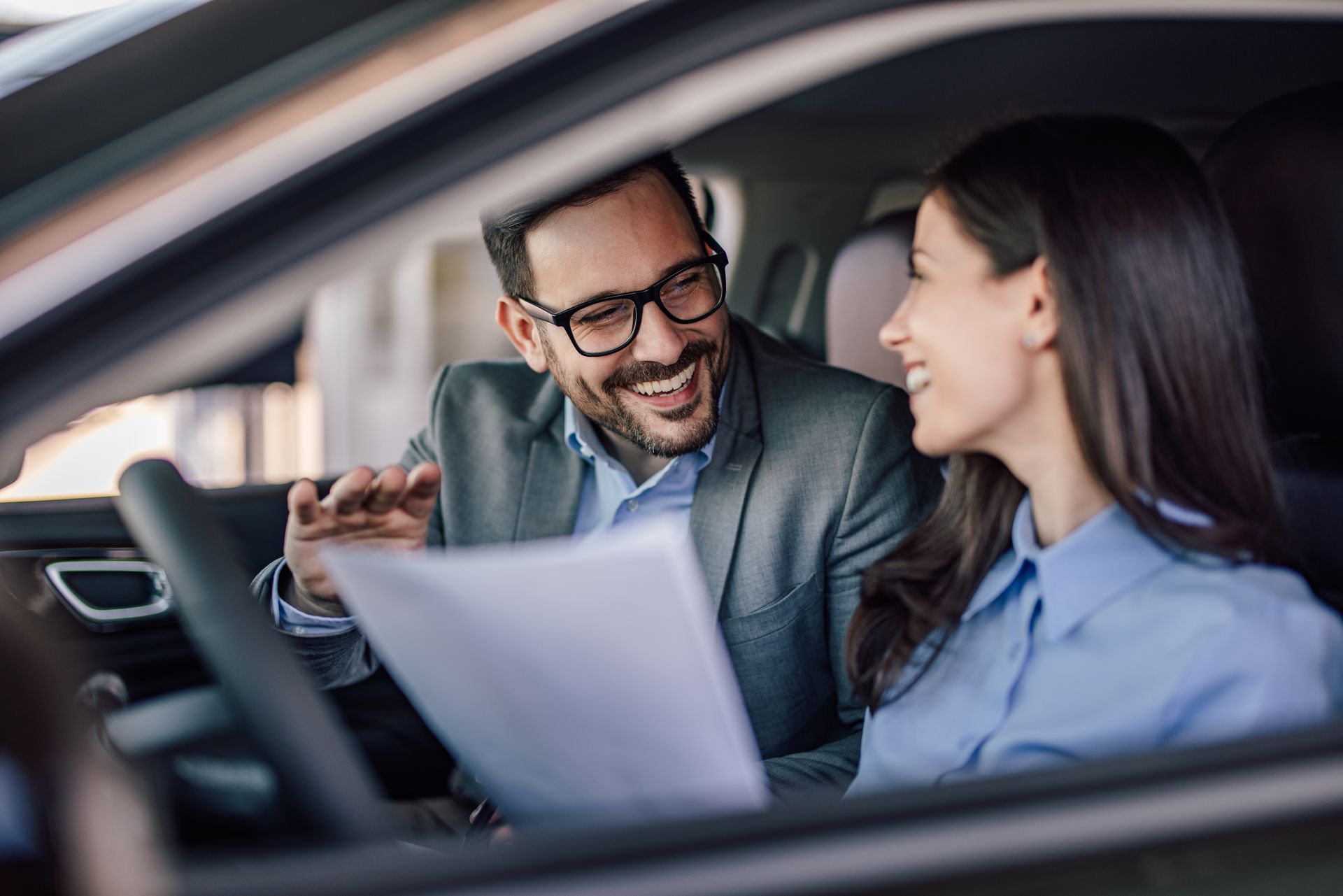 Man in glasses and woman in car discussing documents.