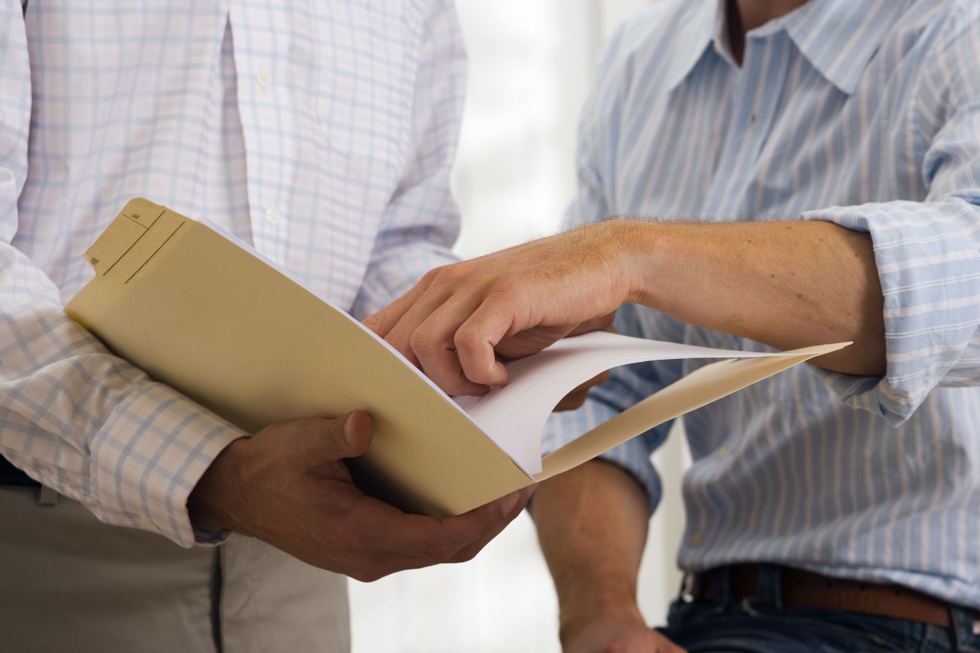 Two men examining documents in a file folder, likely discussing the contents.