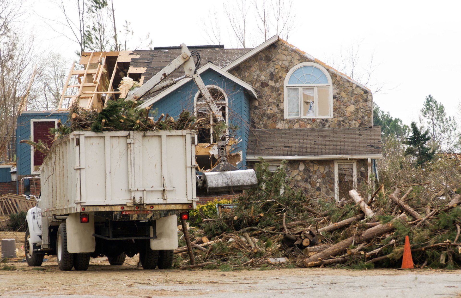 Truck loaded with tree debris in front of a house with roof damage.