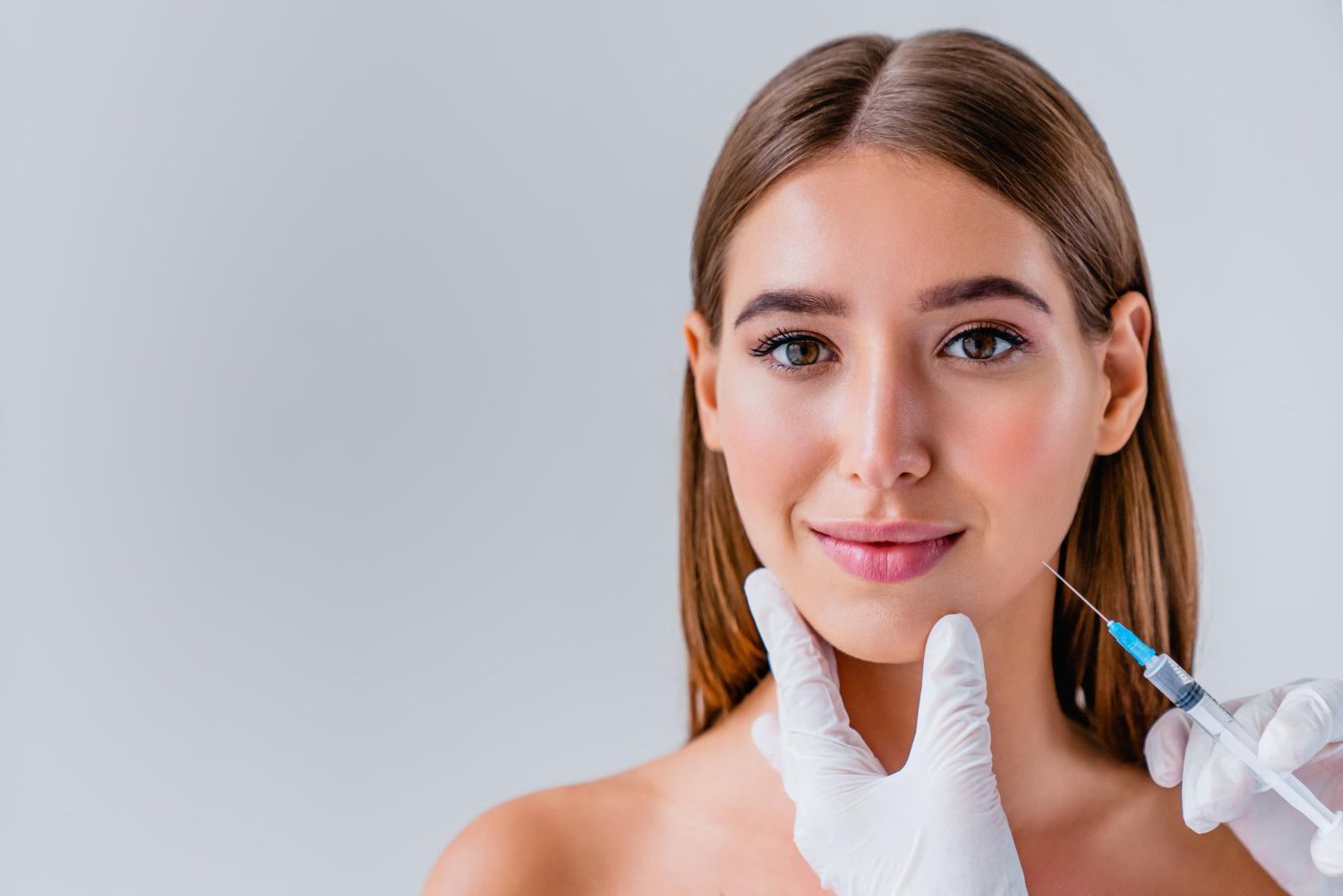 Woman receiving cosmetic facial injection, doctor's gloved hand holding syringe, studio.