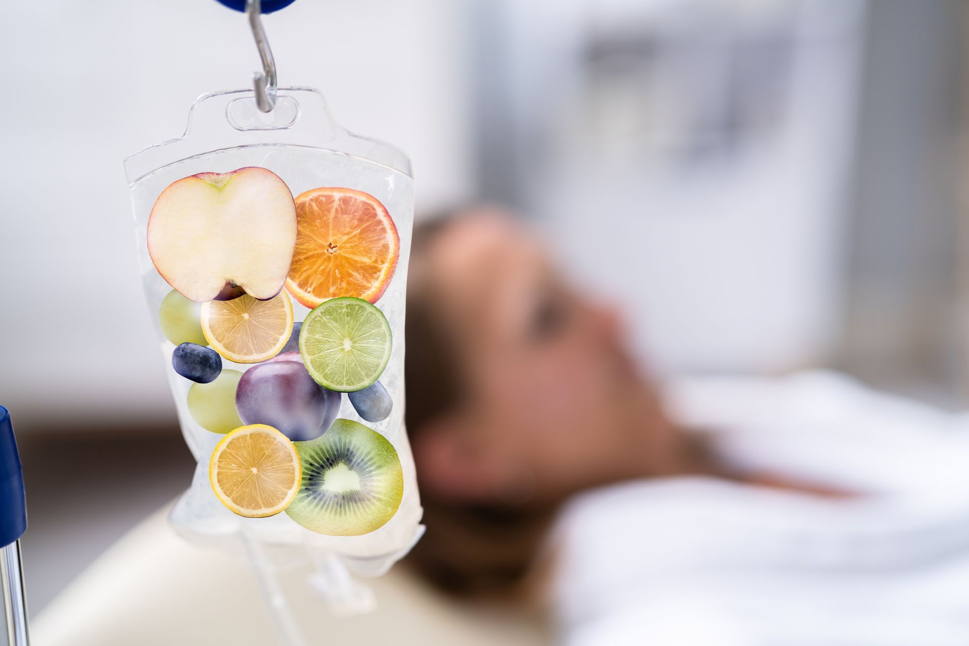 IV bag with mixed fruit hanging above a person in a hospital bed, blurry background.
