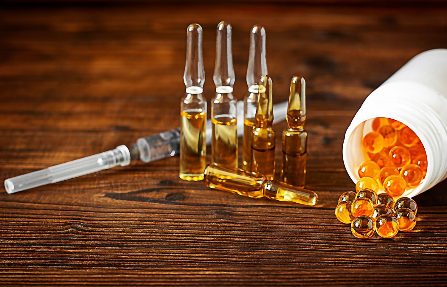 Syringe, vials, and orange capsules on a wooden surface, possibly for medication or health supplements.