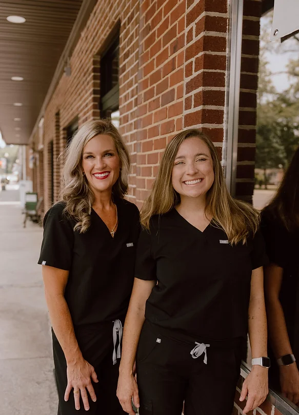 two women in scrubs are standing next to each other in front of a brick building .