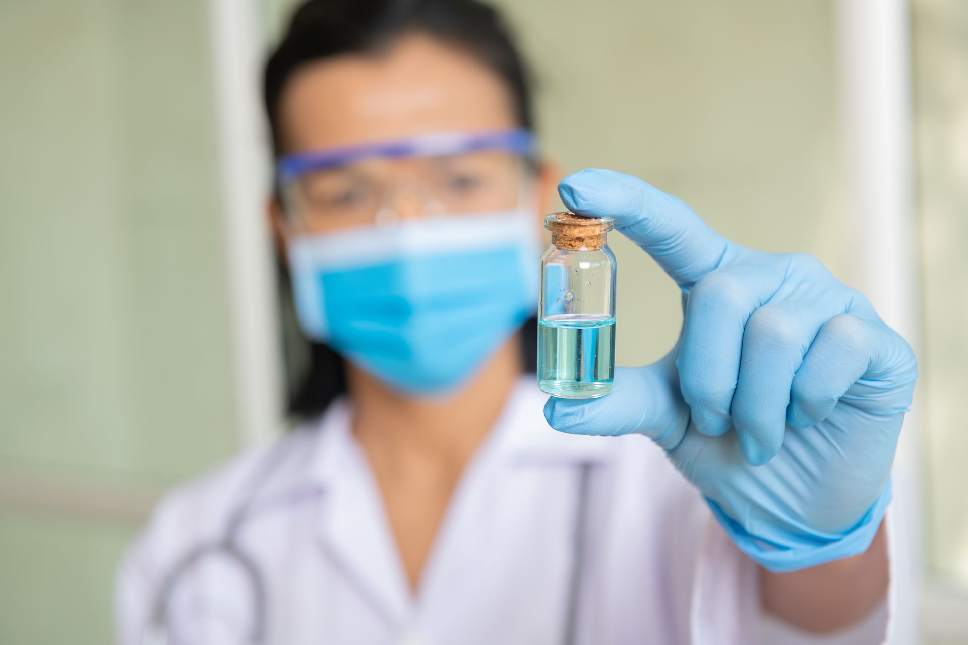 a female doctor wearing a mask and gloves is holding a small bottle of liquid .