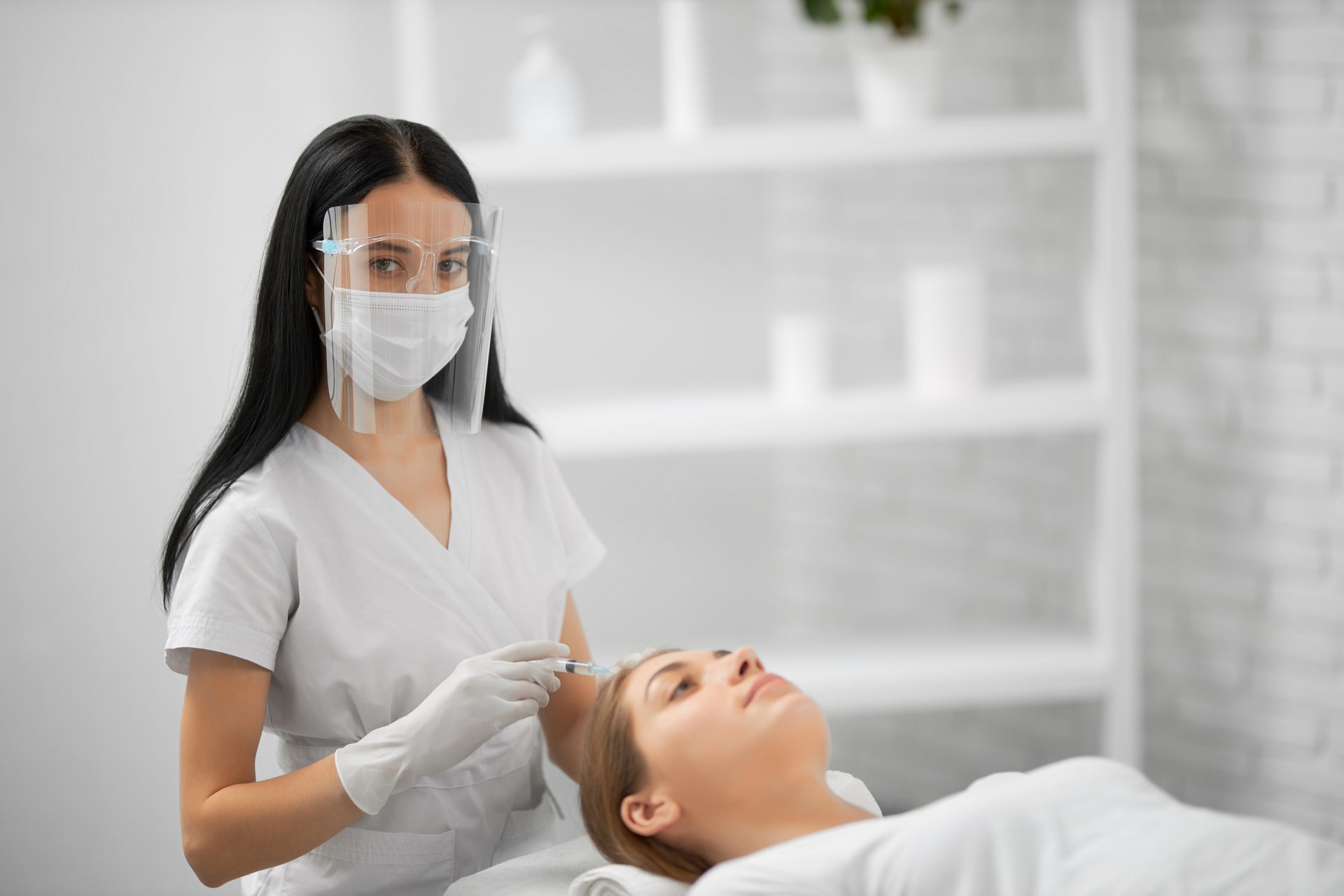 a woman is getting a facial treatment at a beauty salon while wearing a mask and face shield .