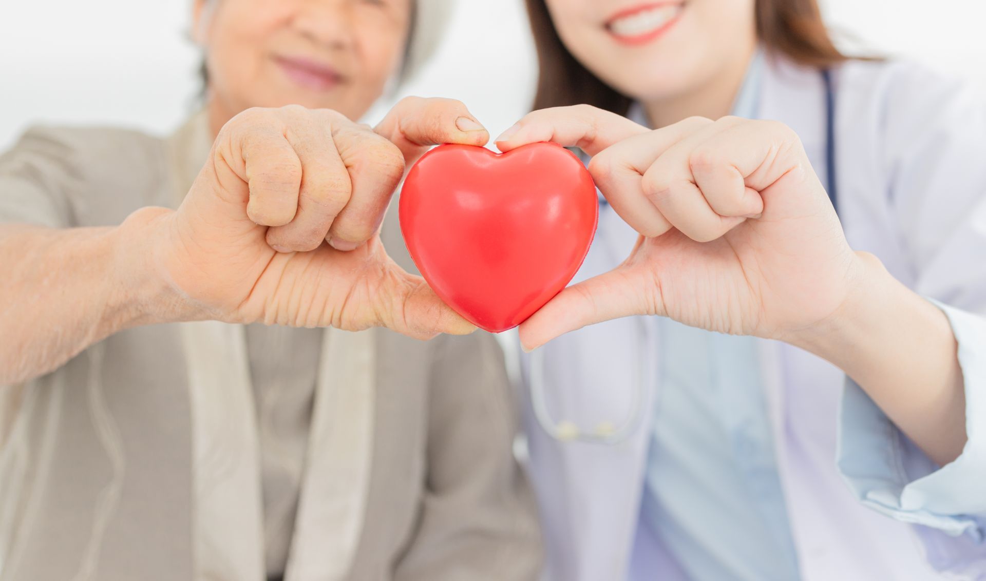 a doctor and an elderly woman are making a heart shape with their hands .