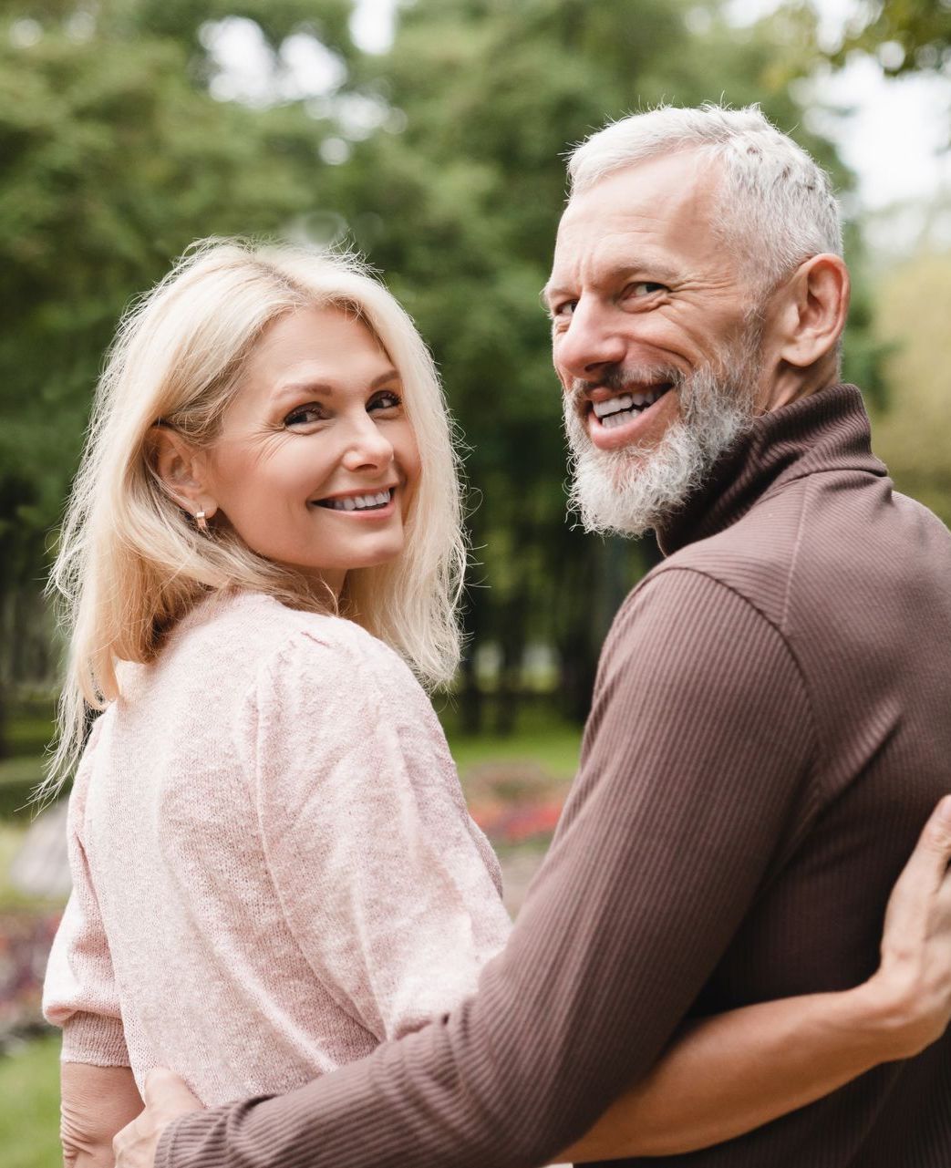 A man and a woman are hugging each other in a park.