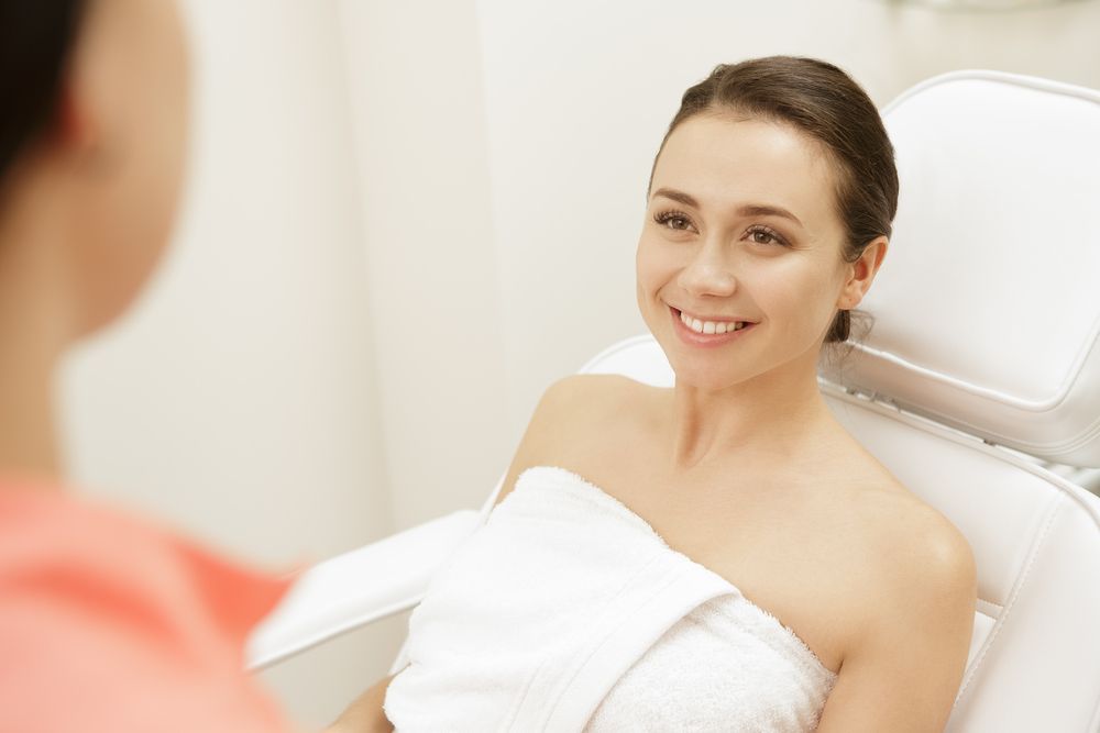 A woman is wrapped in a towel and smiling while sitting in a chair.