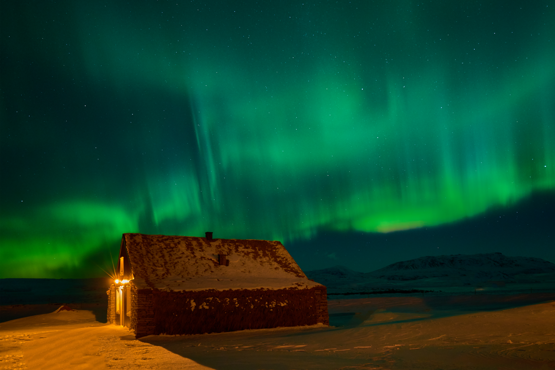 The aurora borealis is shining over a small house in the snow.