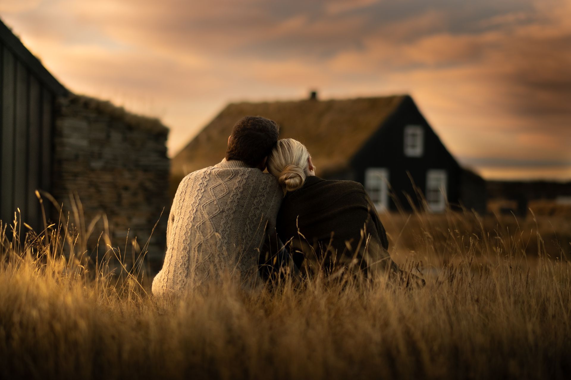 A couple is sitting in a field looking at a house.