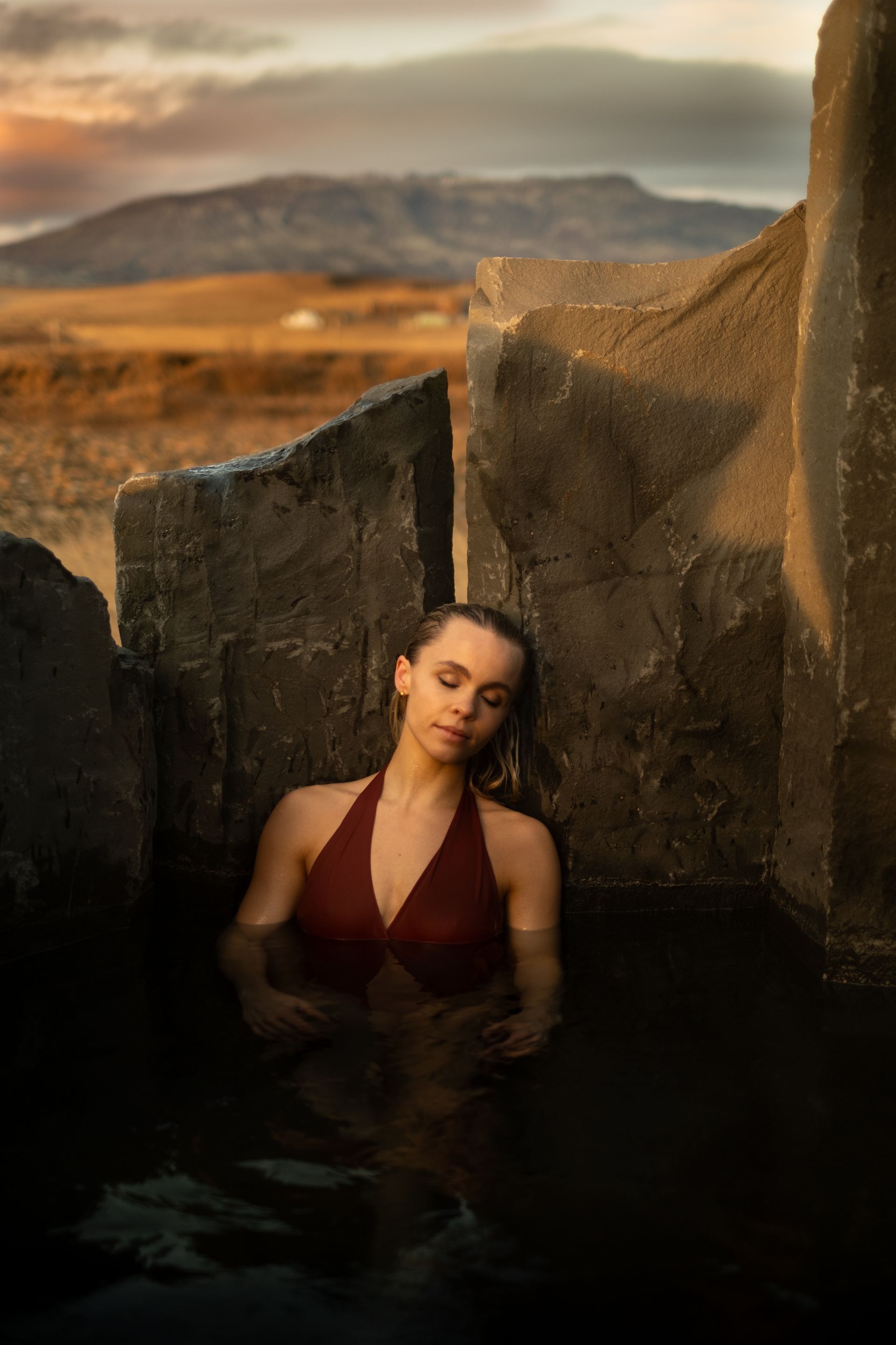 A woman in a red swimsuit is standing in a pool of water surrounded by rocks.