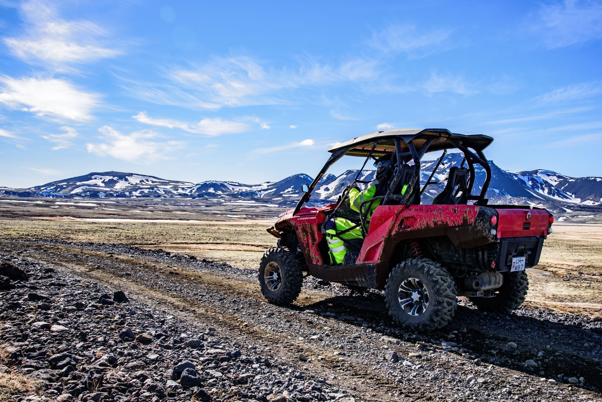 A red atv is driving down a dirt road with mountains in the background.