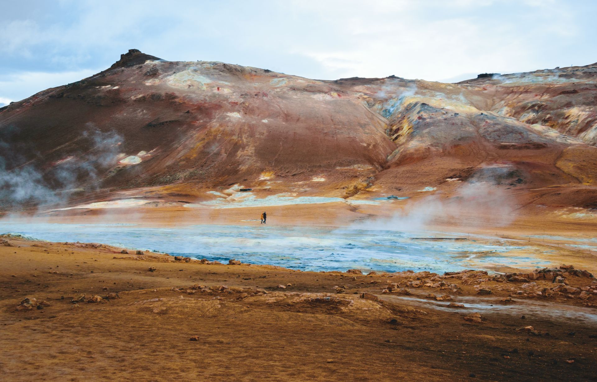 A person is standing in the middle of a desert near a lake.