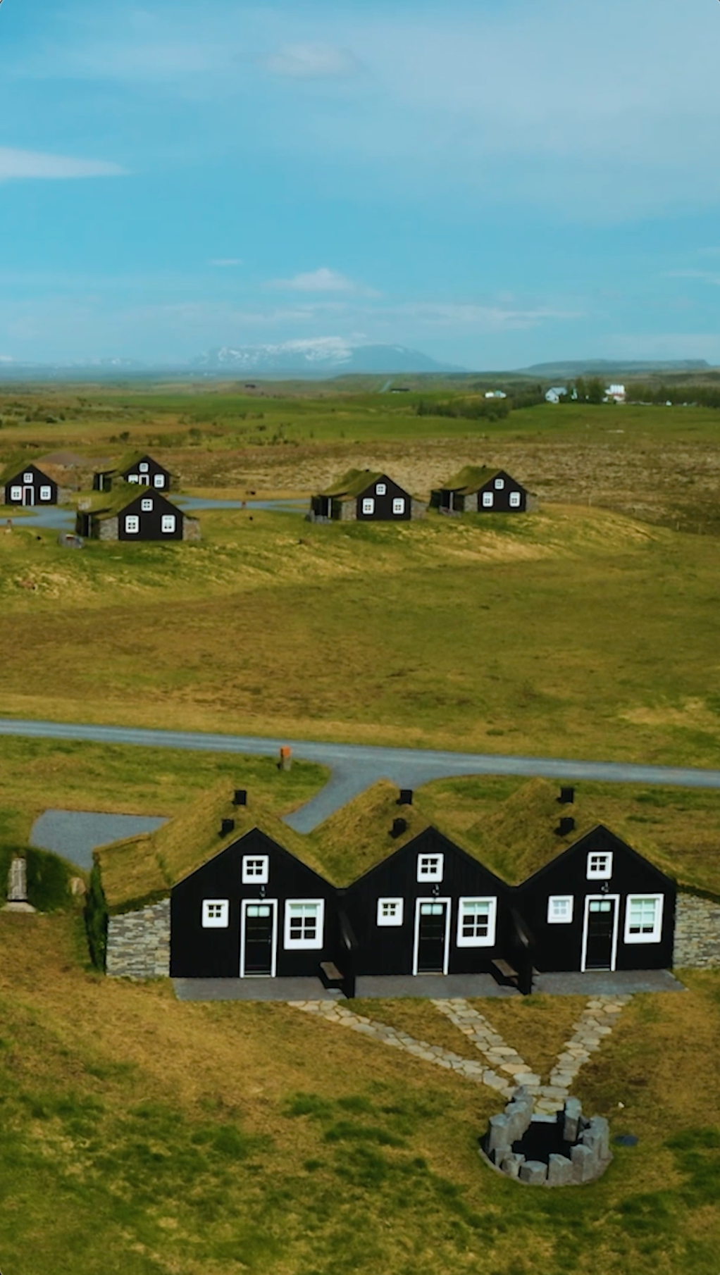A row of black houses with grass on the roofs in a field.