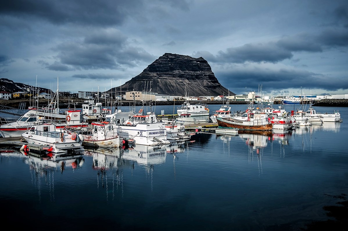 A group of boats are docked in a harbor with a mountain in the background.