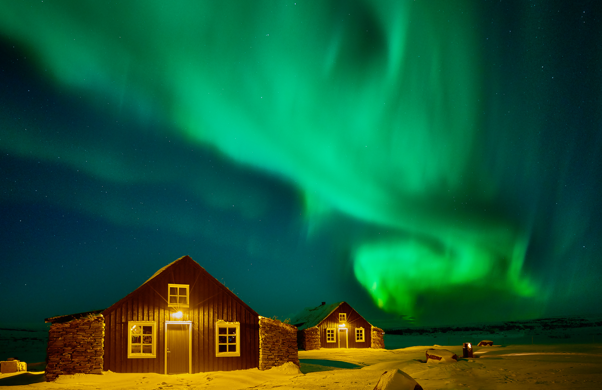 The northern lights are dancing in the night sky over two houses.