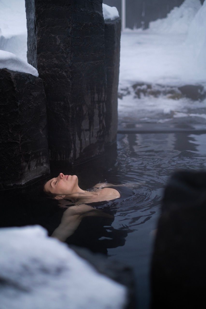 A woman in a red swimsuit is standing in a pool of water surrounded by rocks.