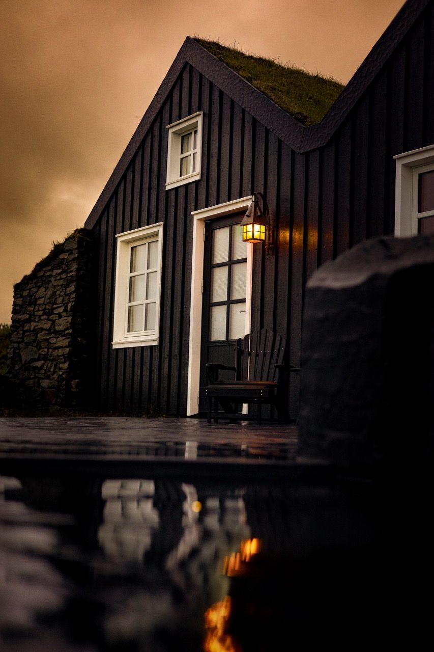A black house with a green roof is reflected in a puddle of water.