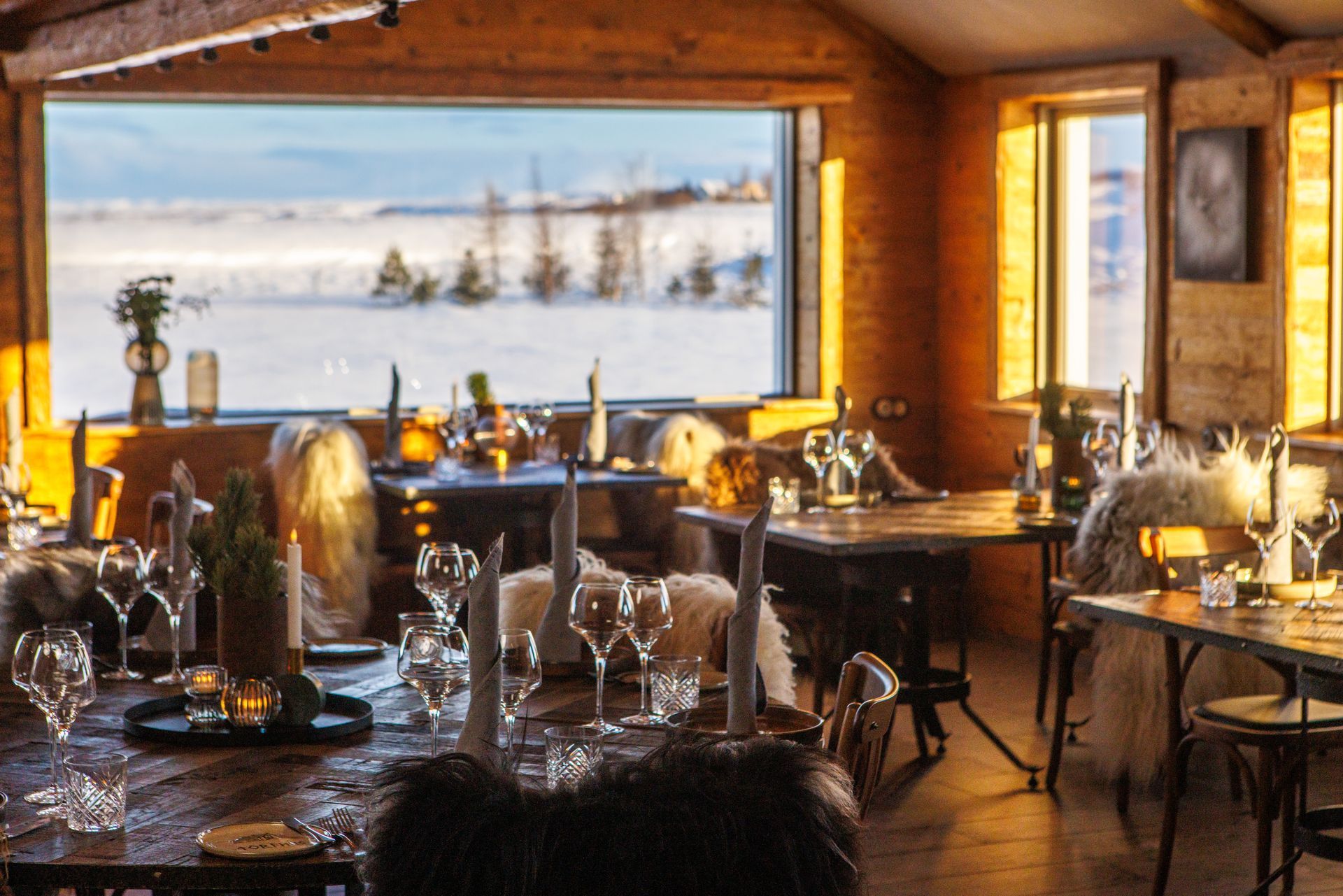 A restaurant with tables and chairs and a large window with a view of the snow.